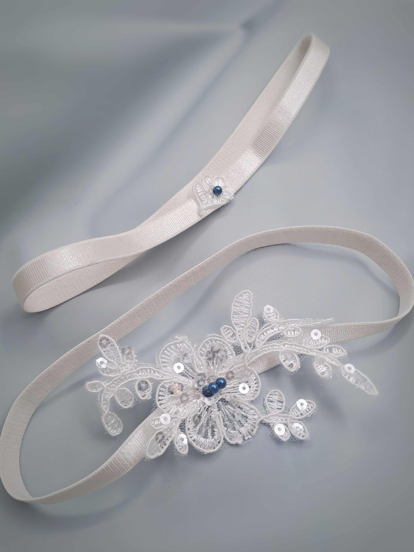 Monaco Bridal Wedding garter set with floral design and blue stones on a gray background