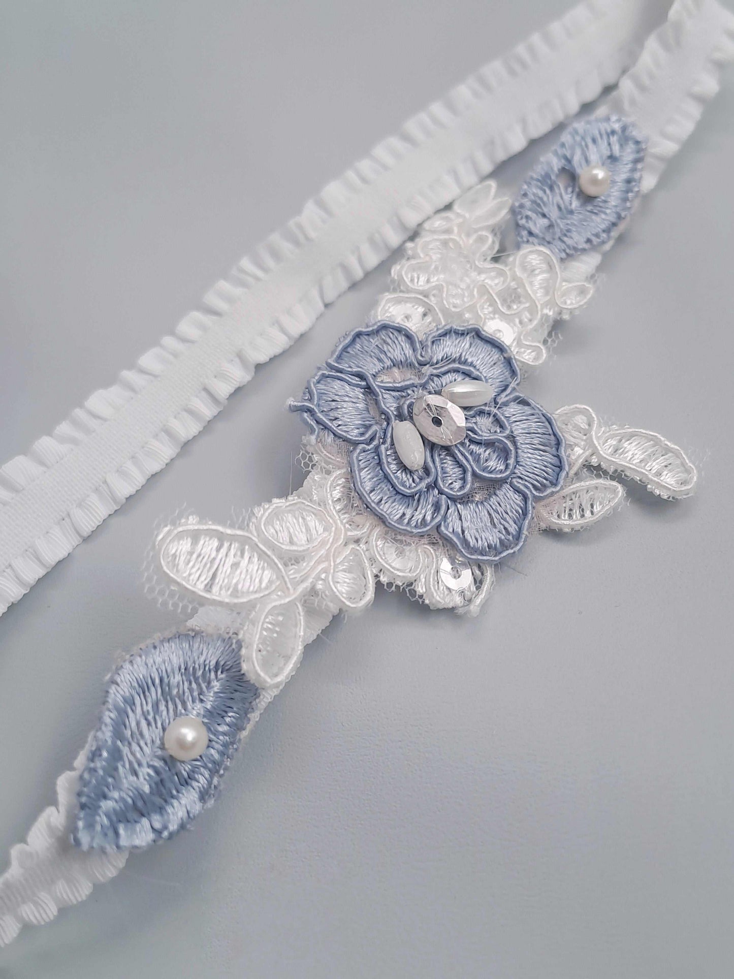 Decorative lace garter with floral embroidery and pearls on a gray background