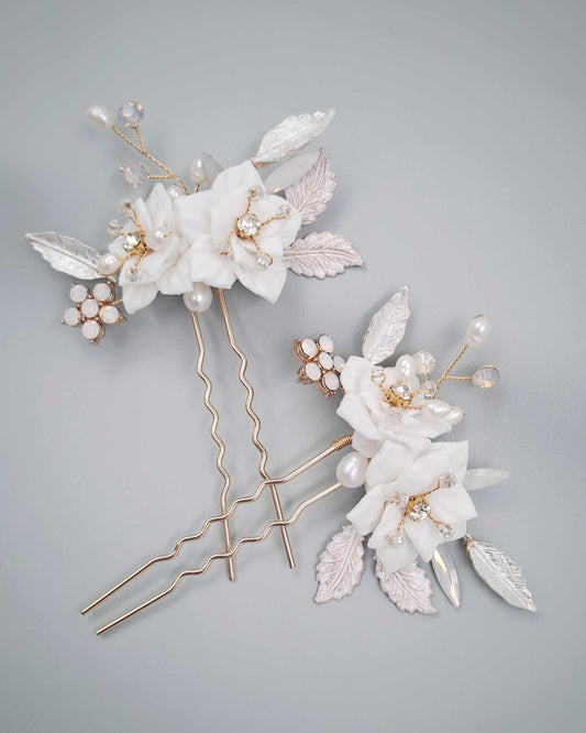 Set of two Val Bridal gold hair pins with white floral details, pearl accents, and rose gold leaves for elegant wedding hairstyles