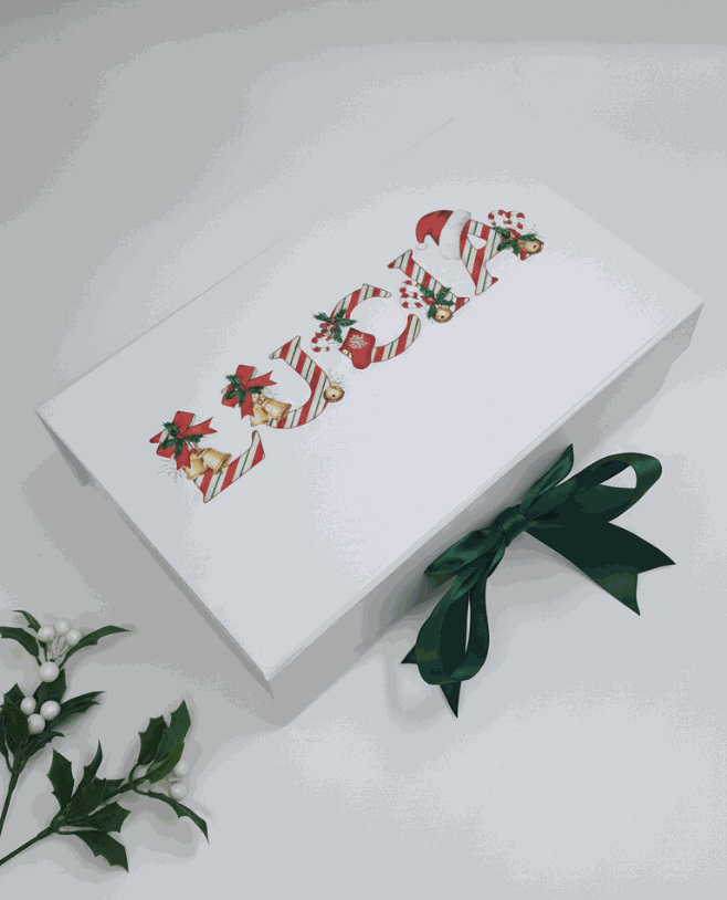 White personaised christmas box with Christmas-themed design and green ribbon on a white background