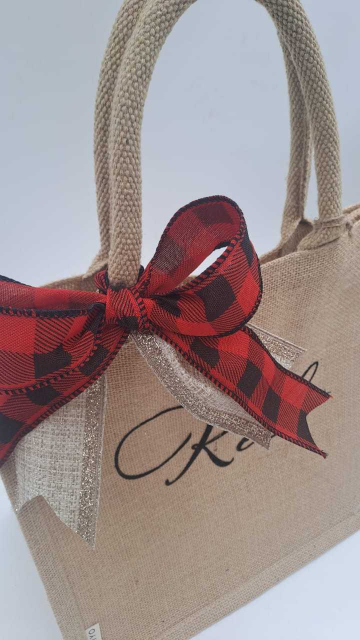 Beach jute tote bag with a red and black plaid christmas bow and 'Kel' text on a light gray background