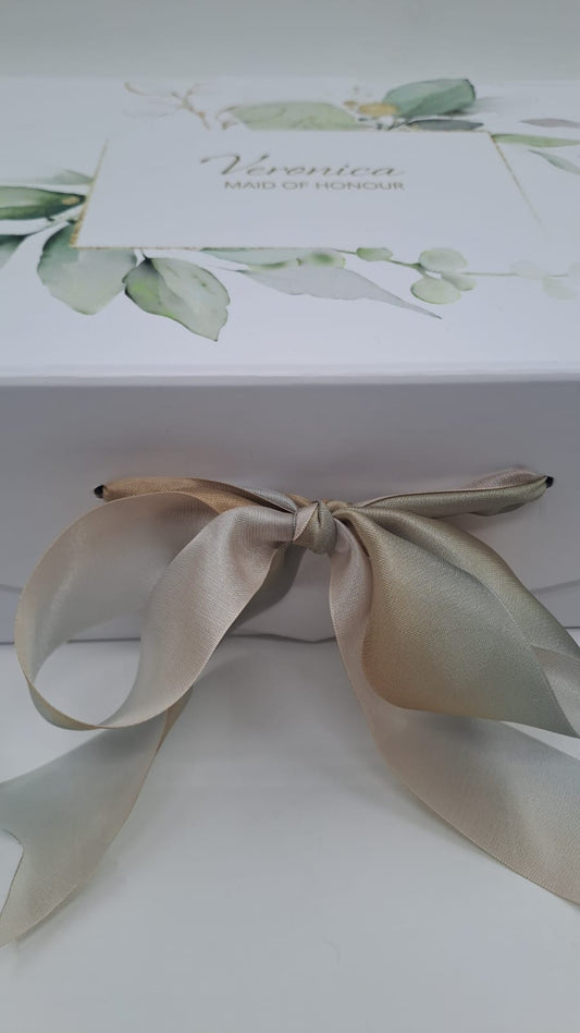 Gift box with a decorative bow and a card featuring greenery on a white background