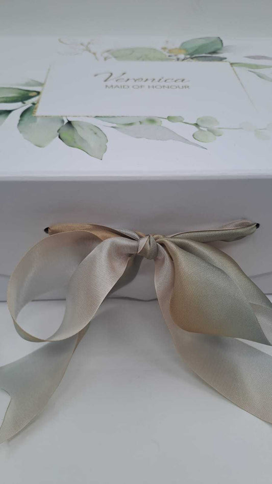 Gift box with a decorative bow and a card featuring greenery on a white background