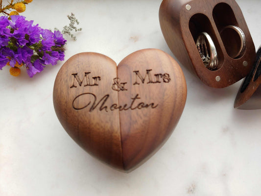 Heart shaped wooden wedding ring box with engraved "Mr & Mrs" and velvet-lined interior holding two rings.