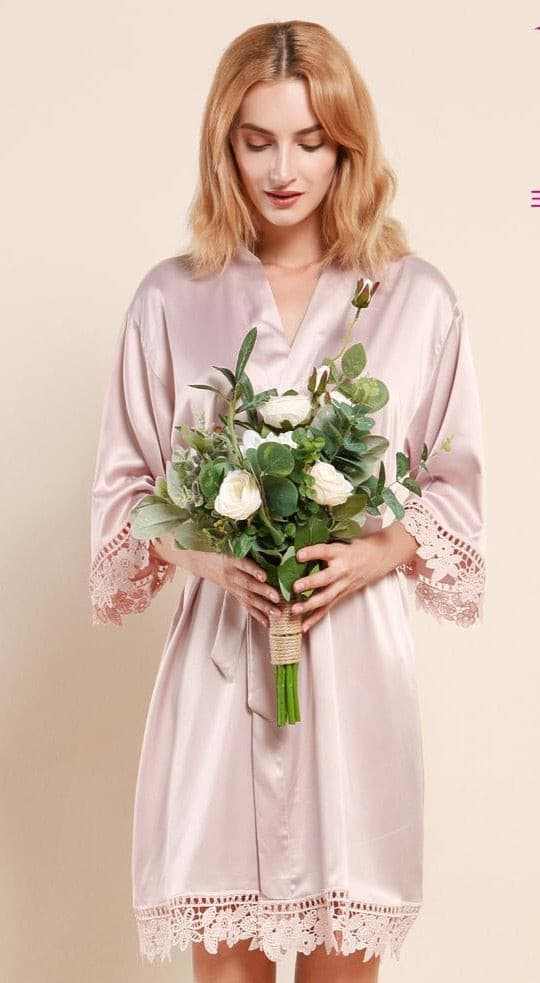 Woman wearing light blush satin robe with lace holding a bouquet of white flowers and greenery