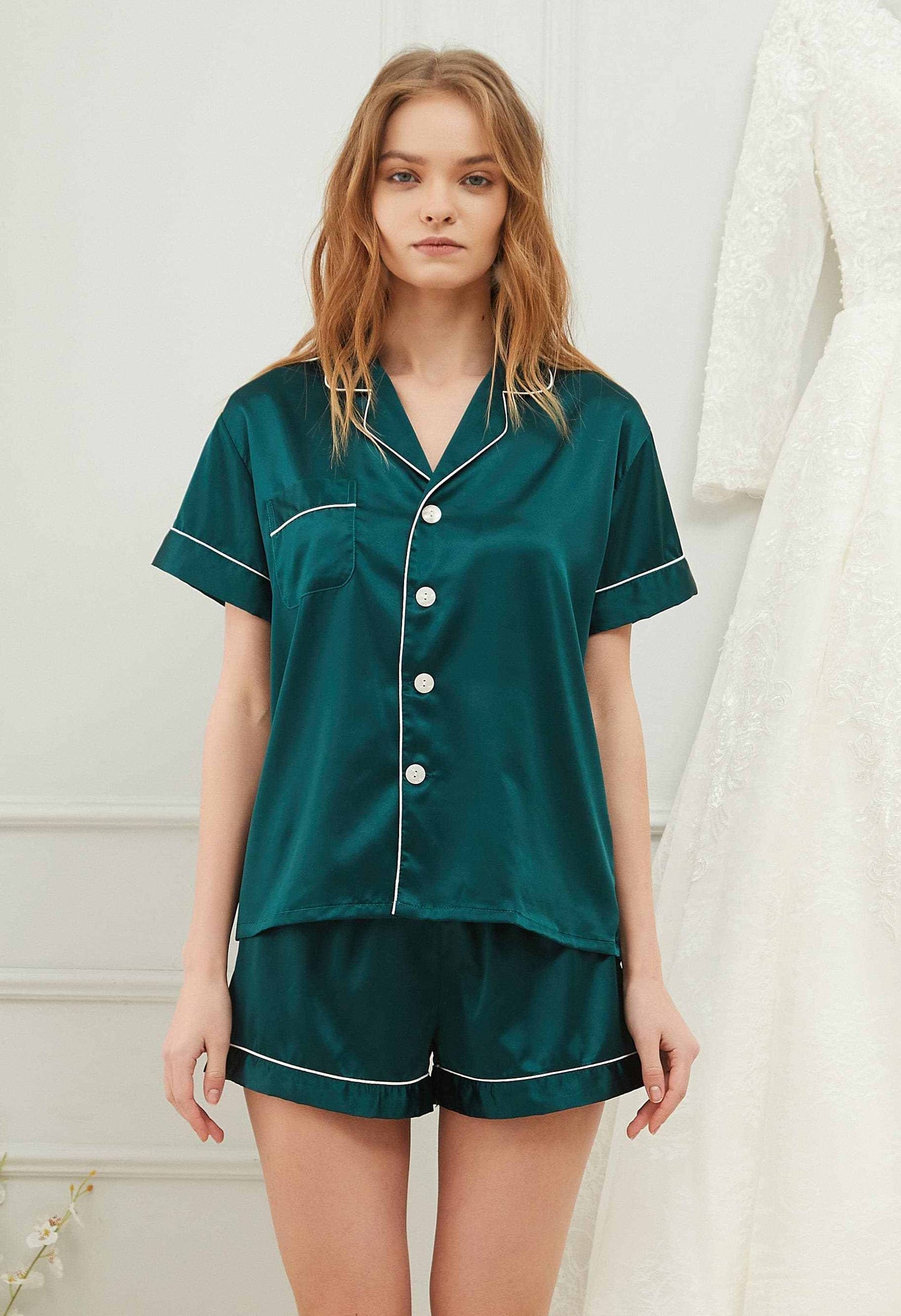 Woman wearing dark green satin short-sleeve pyjama set with button-up top and elastic waistband shorts