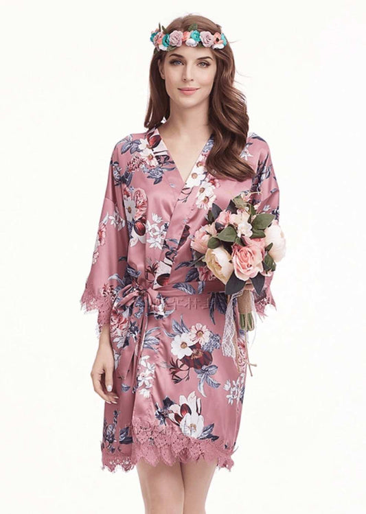 Rose pink satin robe with floral print and lace trim, worn by woman holding bouquet