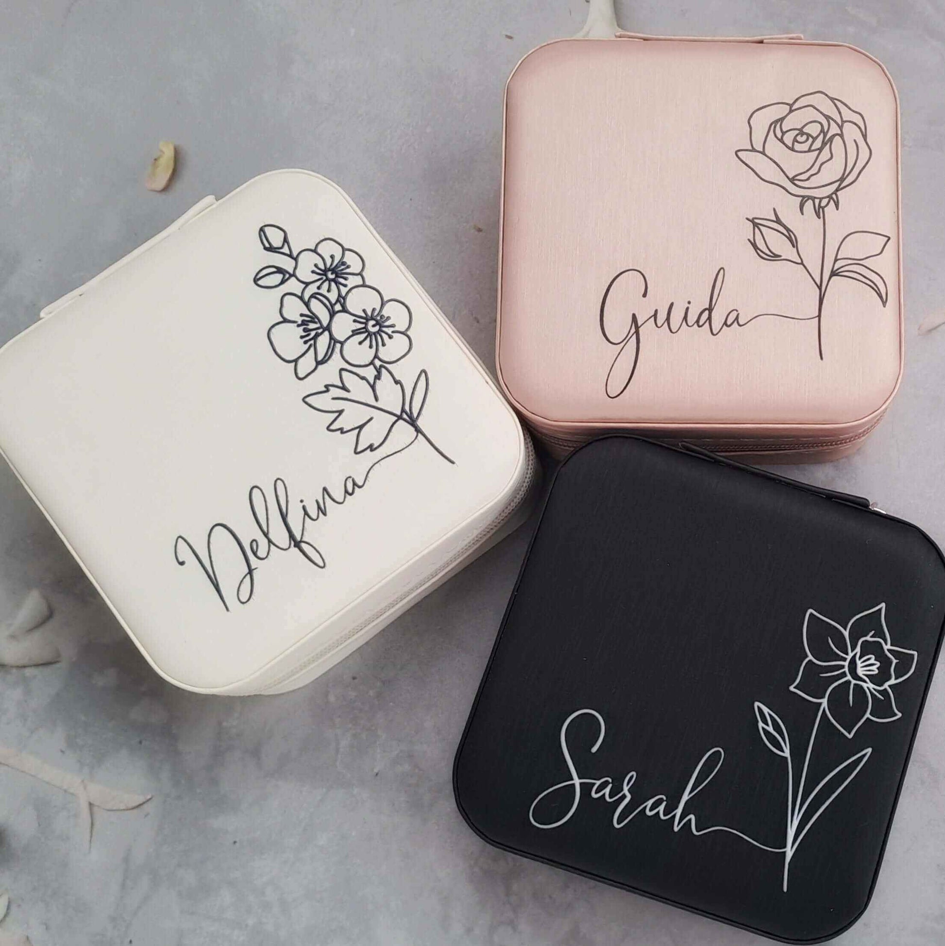 Three spersonalised jewellery boxes with floral designs and names on a gray surface