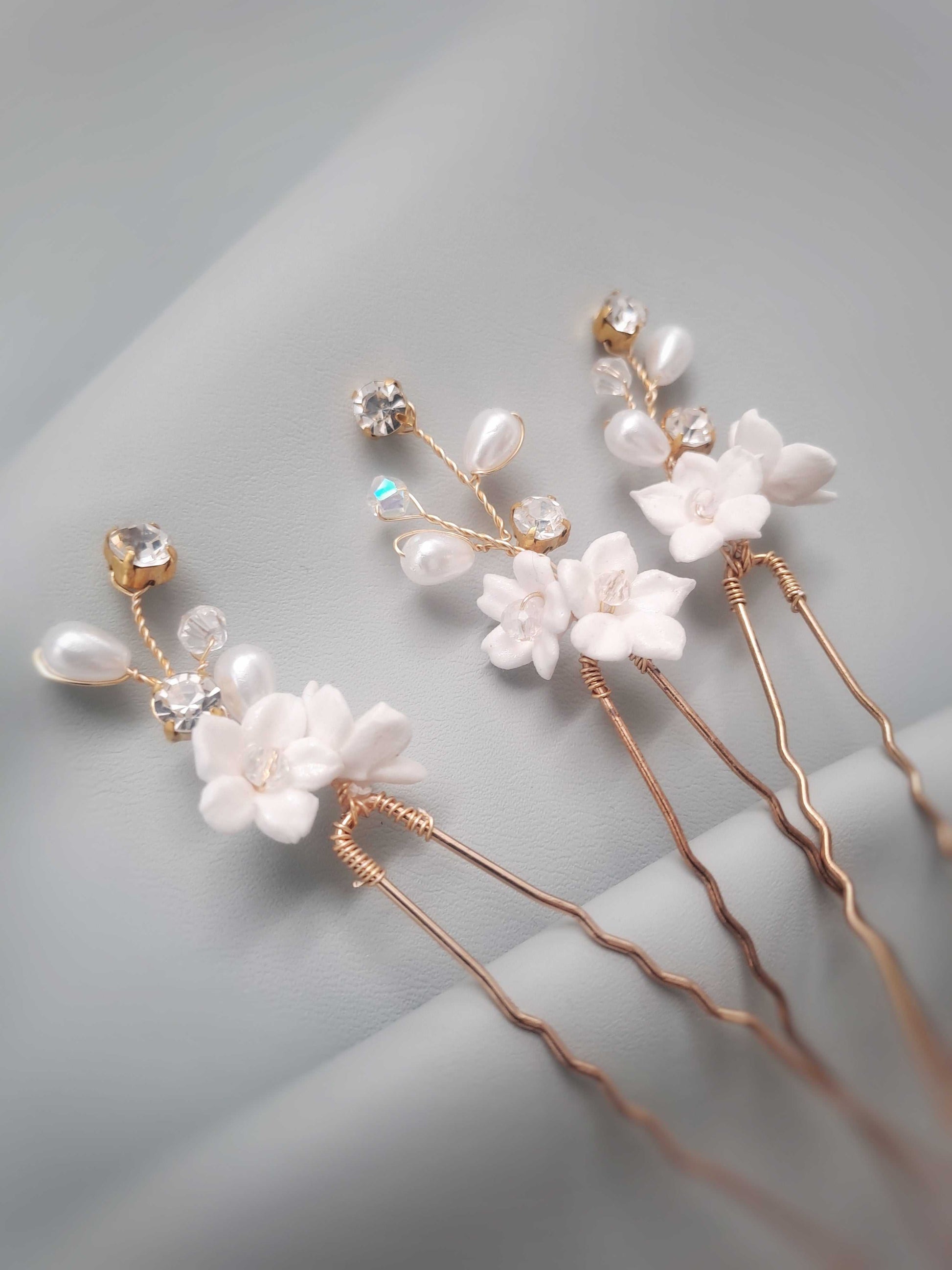 Sienna Bridal Hairpins with white polymer clay flowers, pearls, and crystals in gold tones on a soft gray fabric background