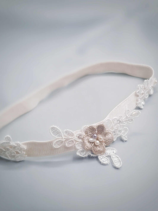 White lace garter with floral embellishments on a light gray background