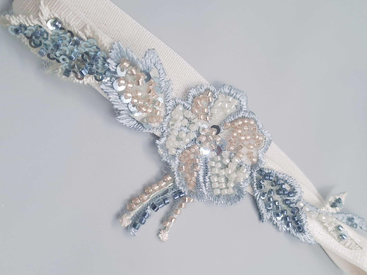 Montrose heirloom wedding garter with hand-beaded champagne, blue, and sage floral design on white band