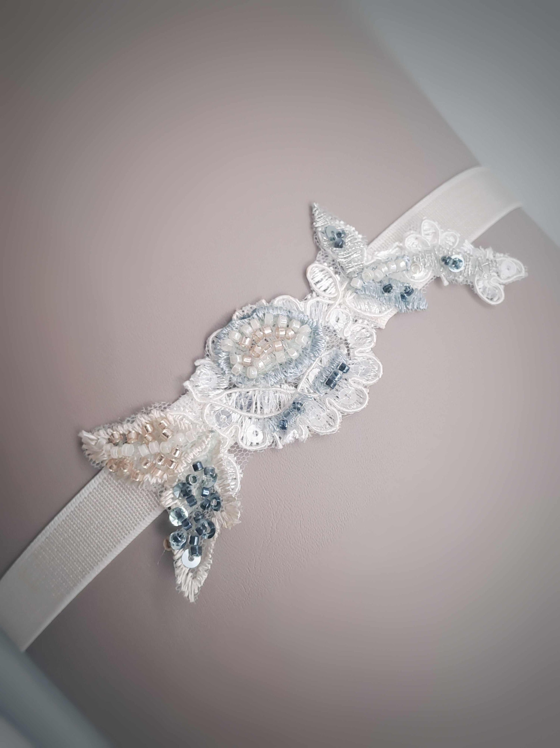 Hand beaded Aspen wedding garter with sage, blue, and champagne beads on white elastic band