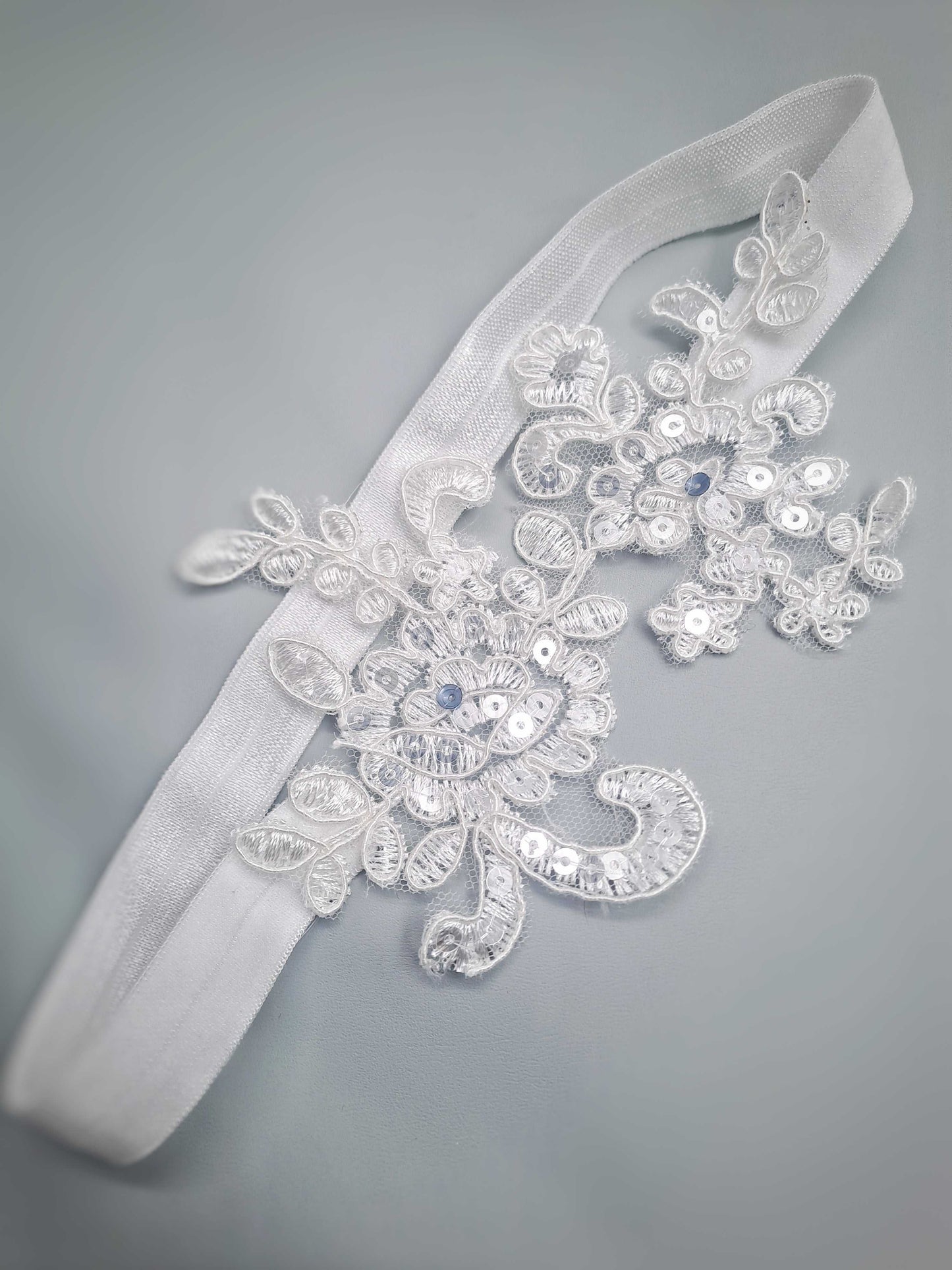 Decorative wedding garter with floral lace and beads on a gray background