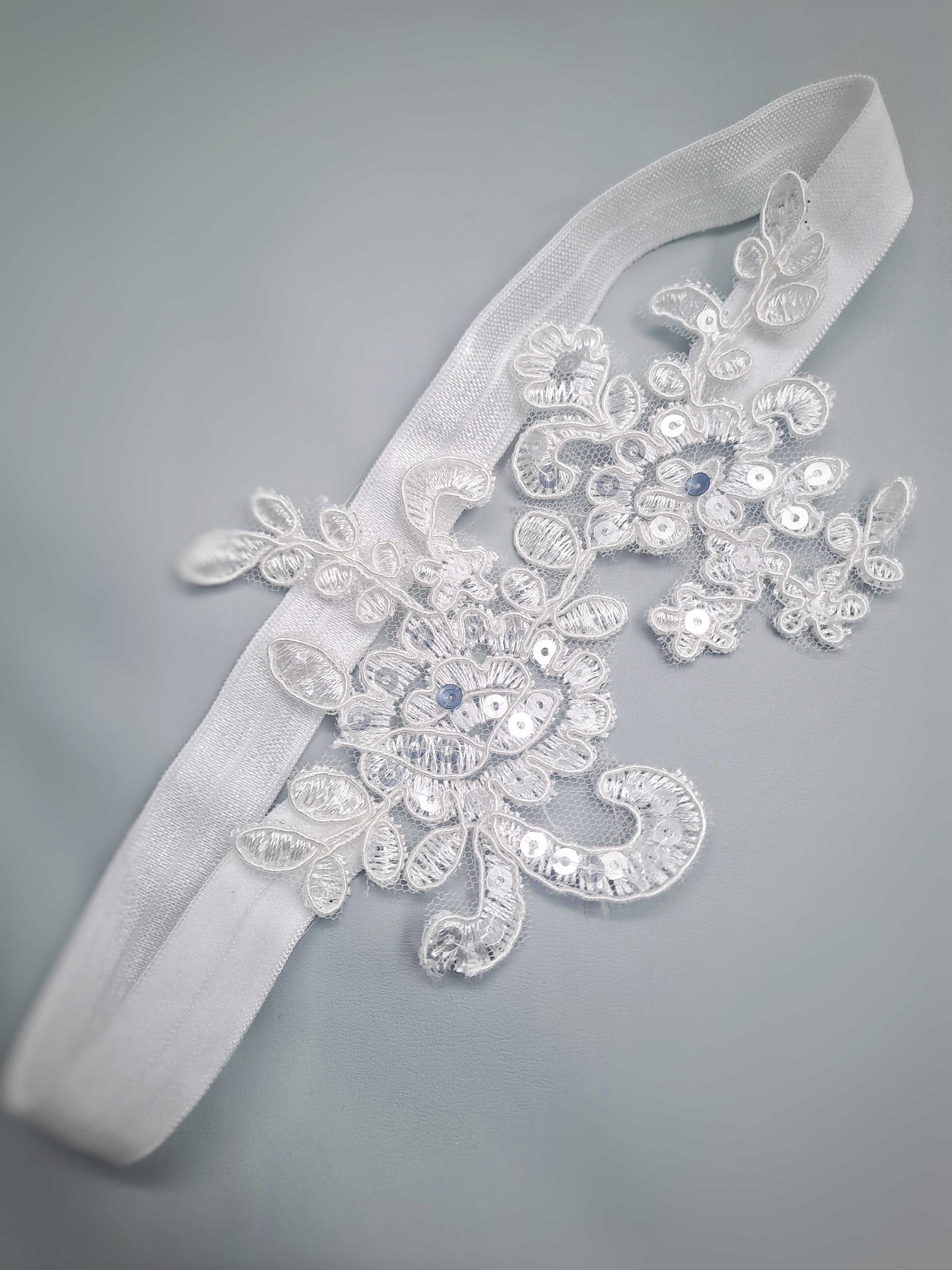 Decorative wedding garter with floral lace and beads on a gray background
