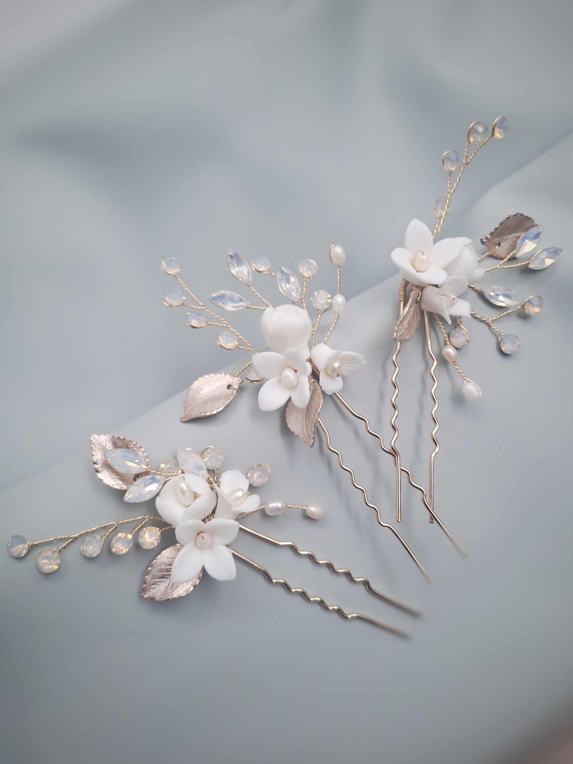 Two floral hairpins with white flowers and gold leaves on a soft gray background
