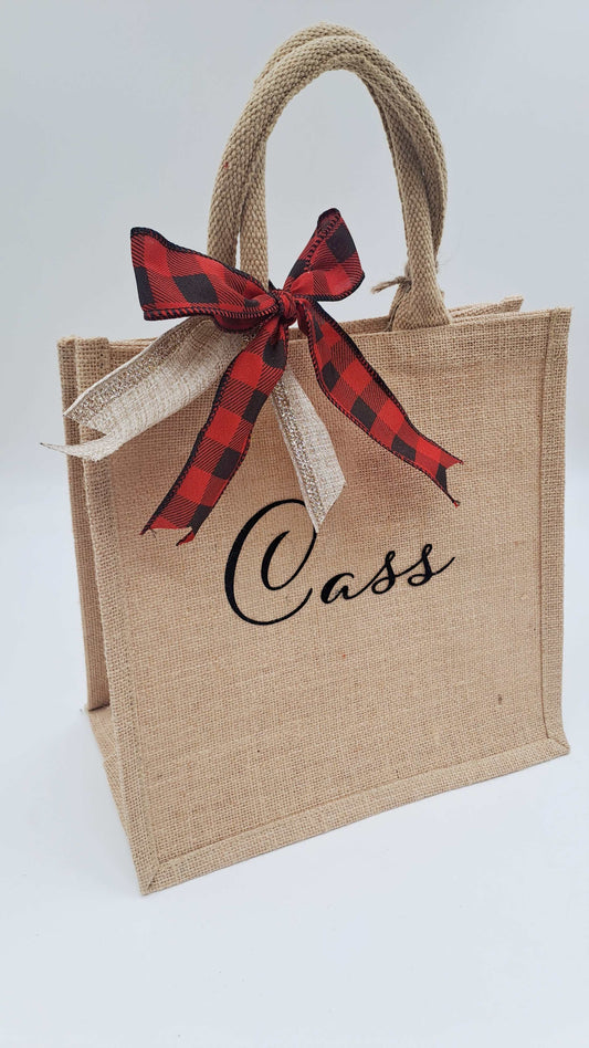 Jute bag with a red and black checkered christmas bow and 'Cass' text on a light gray background