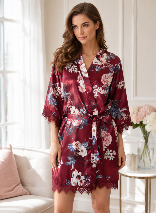 A woman wearing a burgundy satin robe with a pink, white, and blue floral print, standing in a bright, modern bedroom setting.
