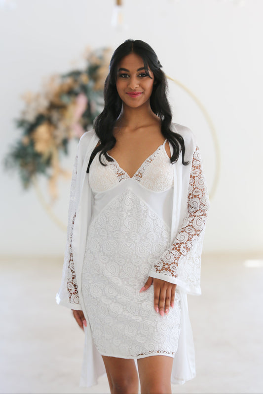 Woman wearing a white lace dress with a long-sleeve cover-up in a decorated indoor setting.