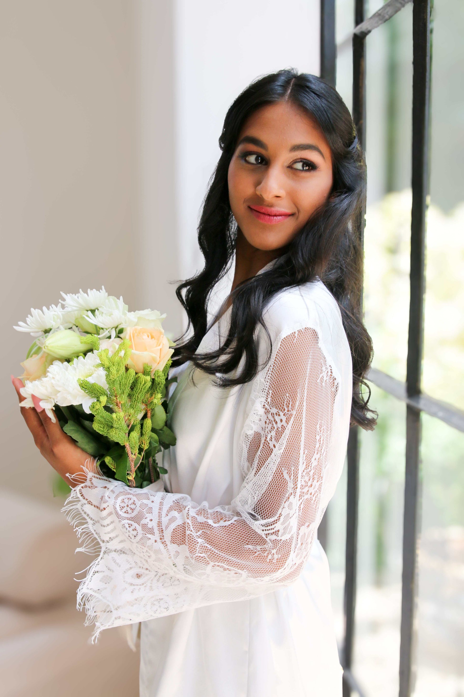 Woman holding a bouquet of flowers in a white lace dress.