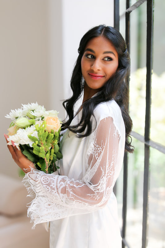 Woman holding a bouquet of flowers in a white lace dress.