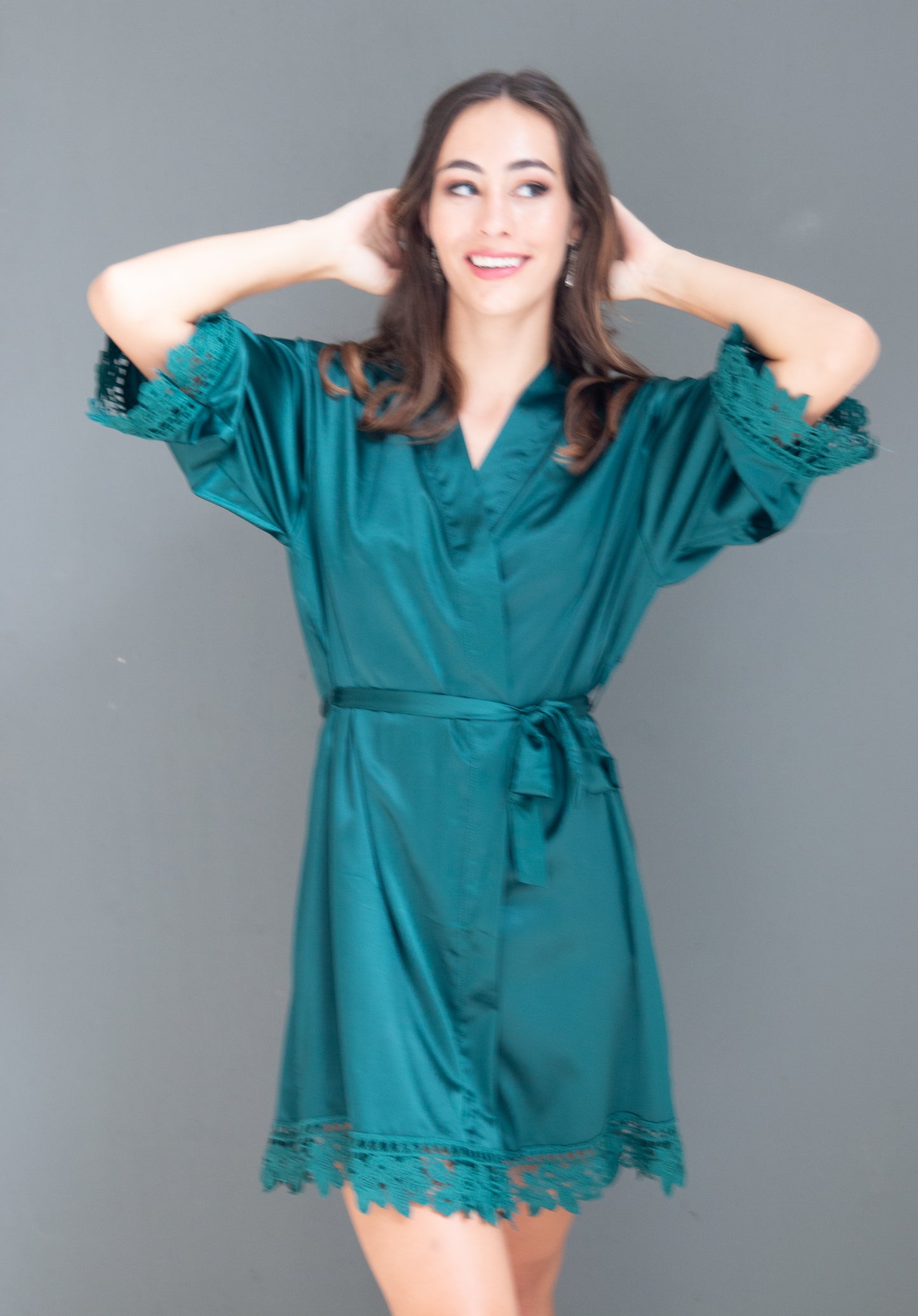 Model wearing an emerald green satin gown with lace trim in the same colour