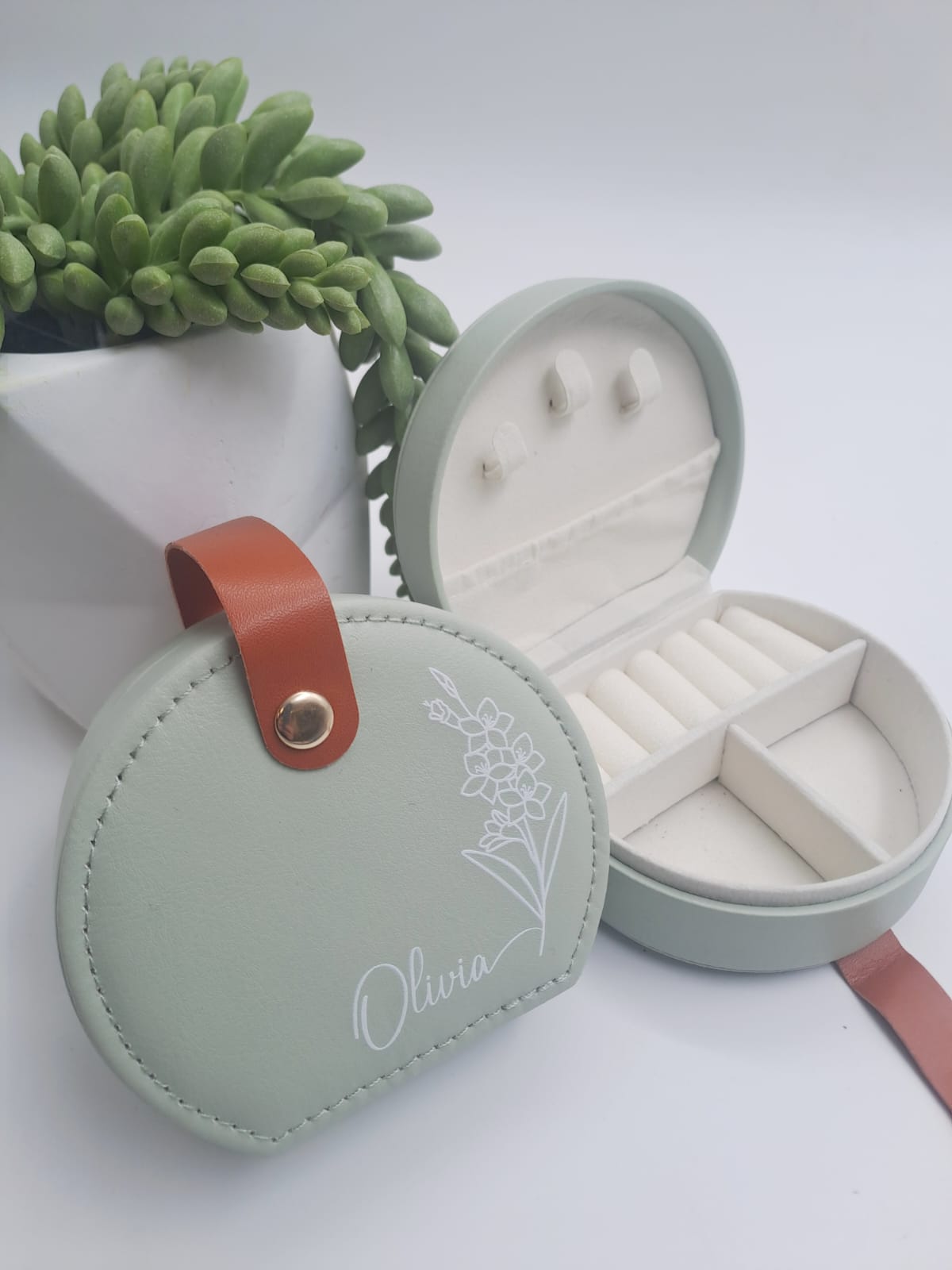 Green jewelry box with a leather strap on a white surface with a plant in the background