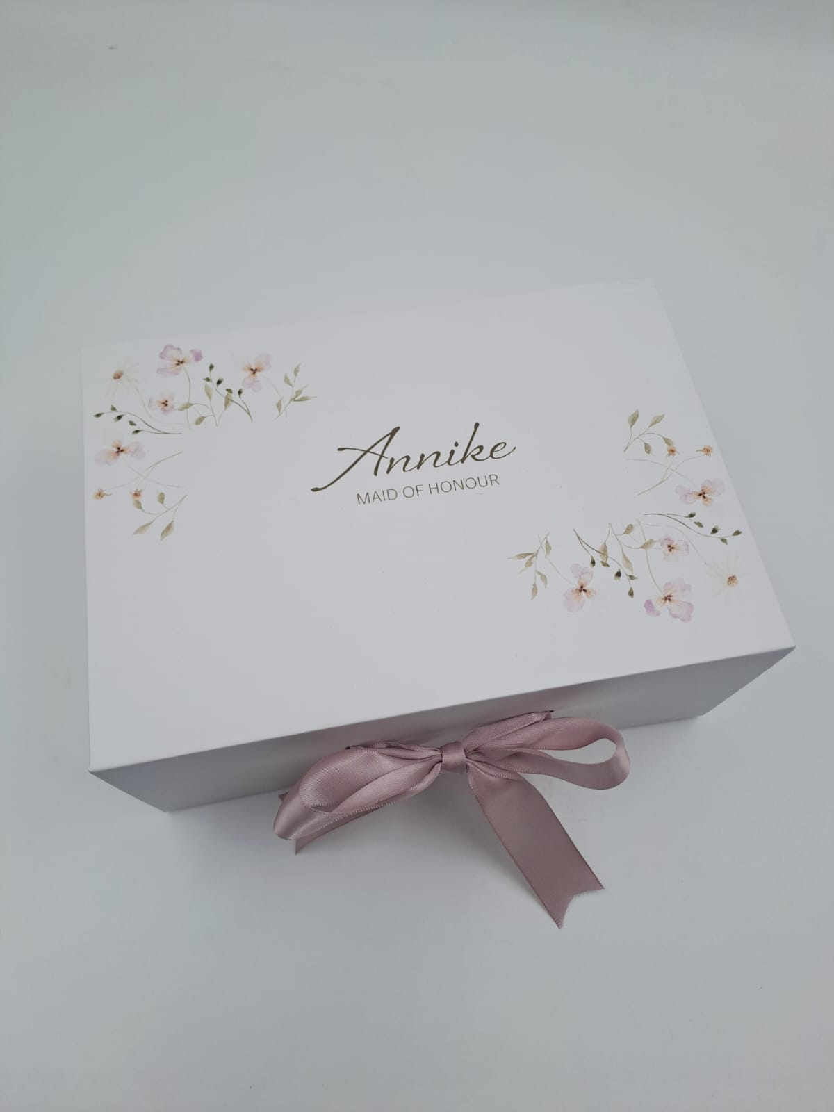 White box with floral design and pink ribbon on a light gray background